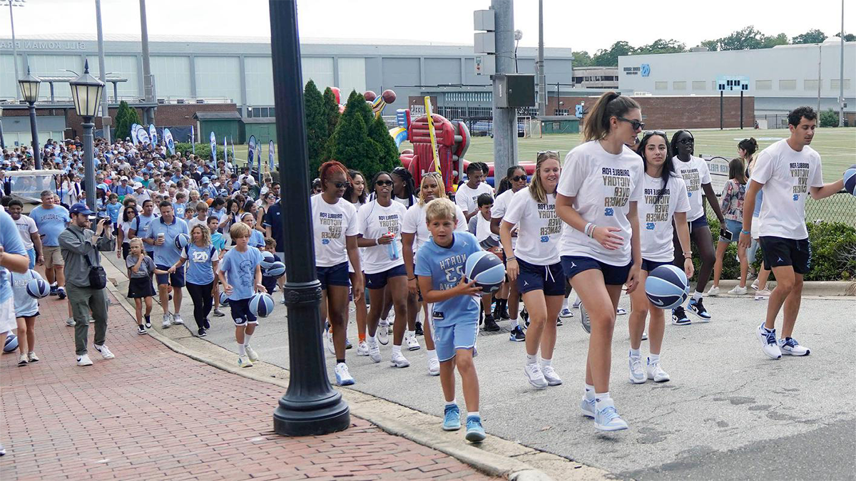 Basketball players and community members walking and dribbling basketballs across campus as part of an event to raise money for pediatric cancer research.