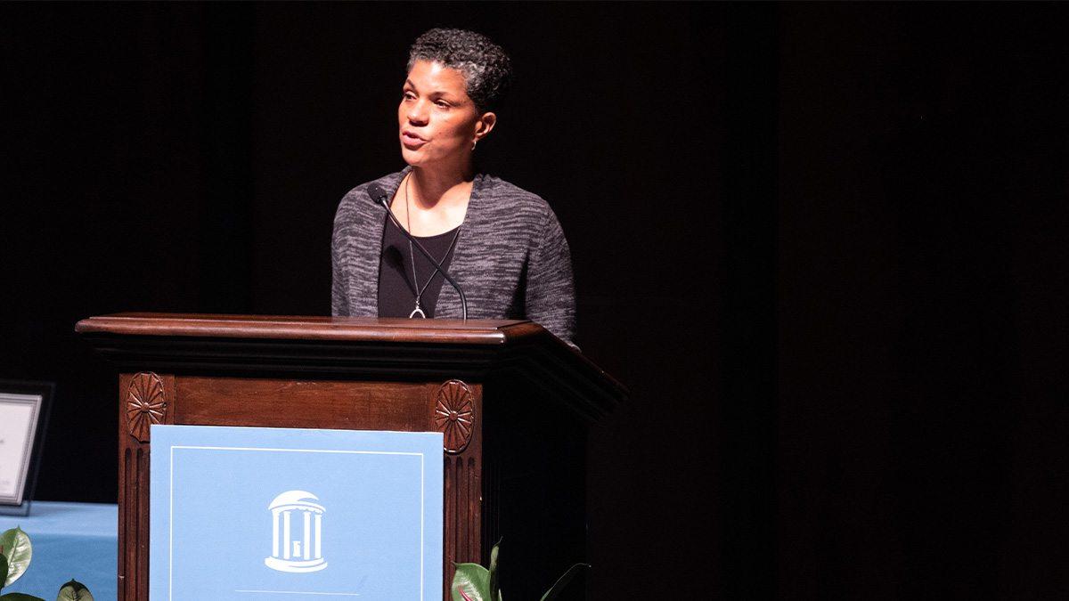 A woman, Michelle 亚历山大, speaking from a podium on a stage at a lecture.