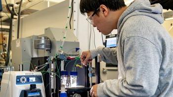 Hueynwoo Yang wearing grey sweatshirt and filling liquid vials with machinery.