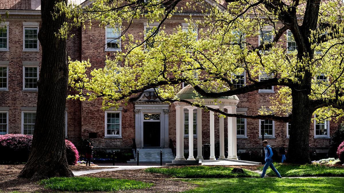 Wide-angle shot of the Old Well on the campus of UNC-Chapel山 with a student walking by it. 南楼在背景中.