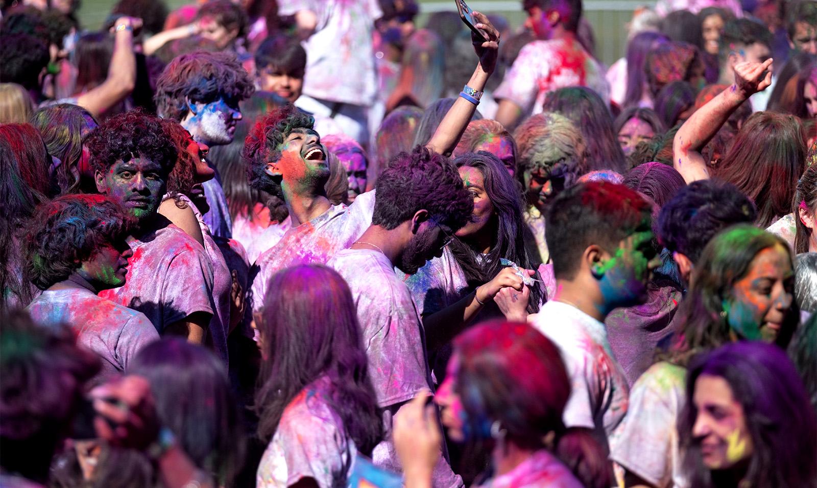 Crowd of students covered in paint celebrating Holi.