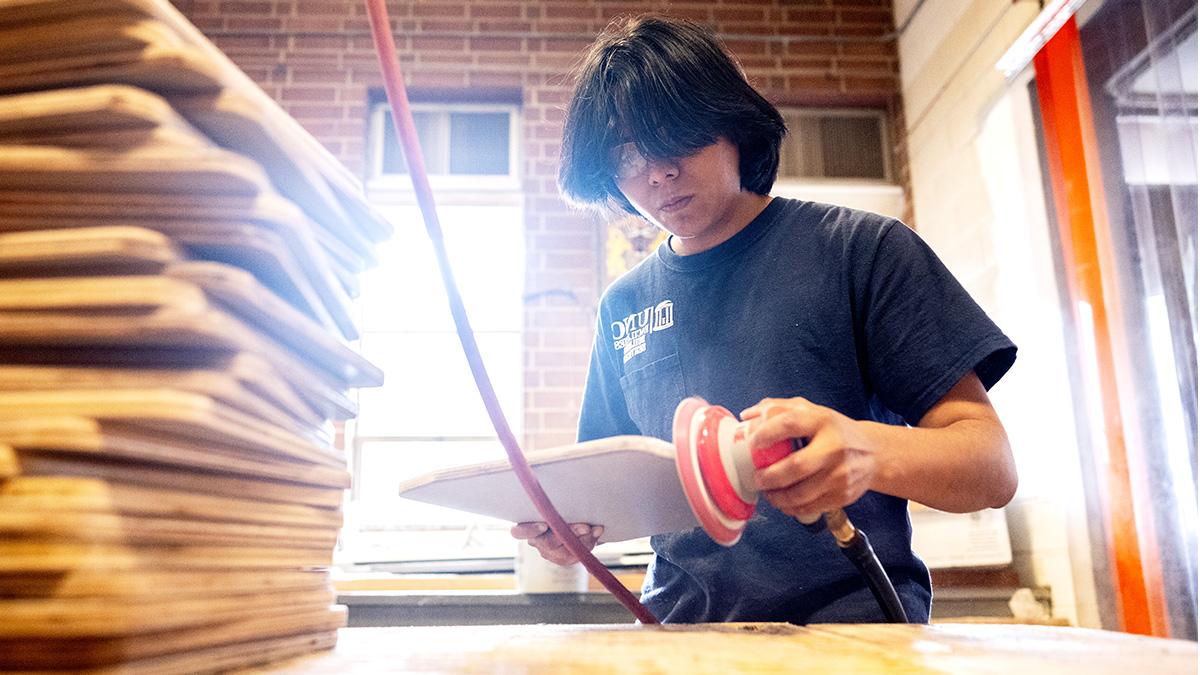 Alex Escobedo wearing safety goggles and sanding objects in the UNC carpentry shop.